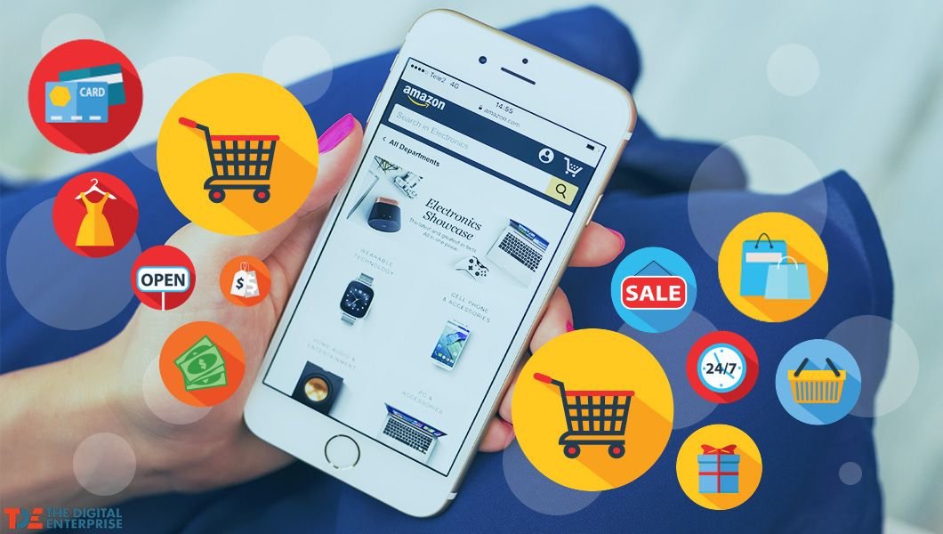 A person is holding a smartphone displaying the Amazon shopping app. The phone is surrounded by various e-commerce related icons, including shopping carts, credit cards, shopping bags, a "SALE" sign, and a 24/7 clock, illustrating the concept of online shopping and digital enterprise.